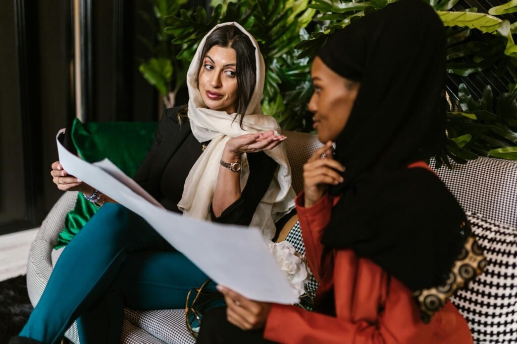 Two women in hijabs engage in a professional discussion while sitting indoors.